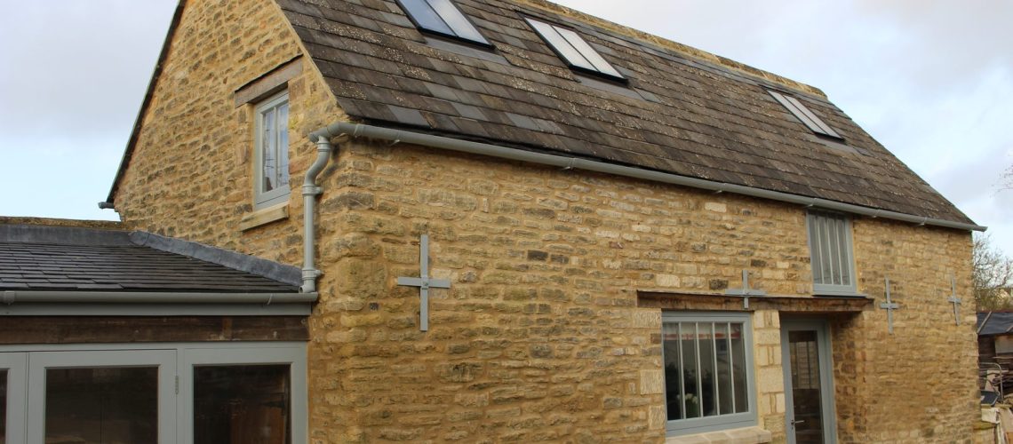 Three small conservation rooflights in the slate roof of a two-storey Bath stone cottage, painted rainwater goods at the eaves