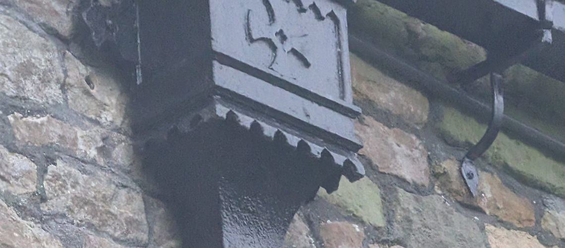 Close up of an ornamental Gothic cast iron hopper head with castellated top, foliate motif and dentil base on a rubble stone church wall, photographed during a site survey